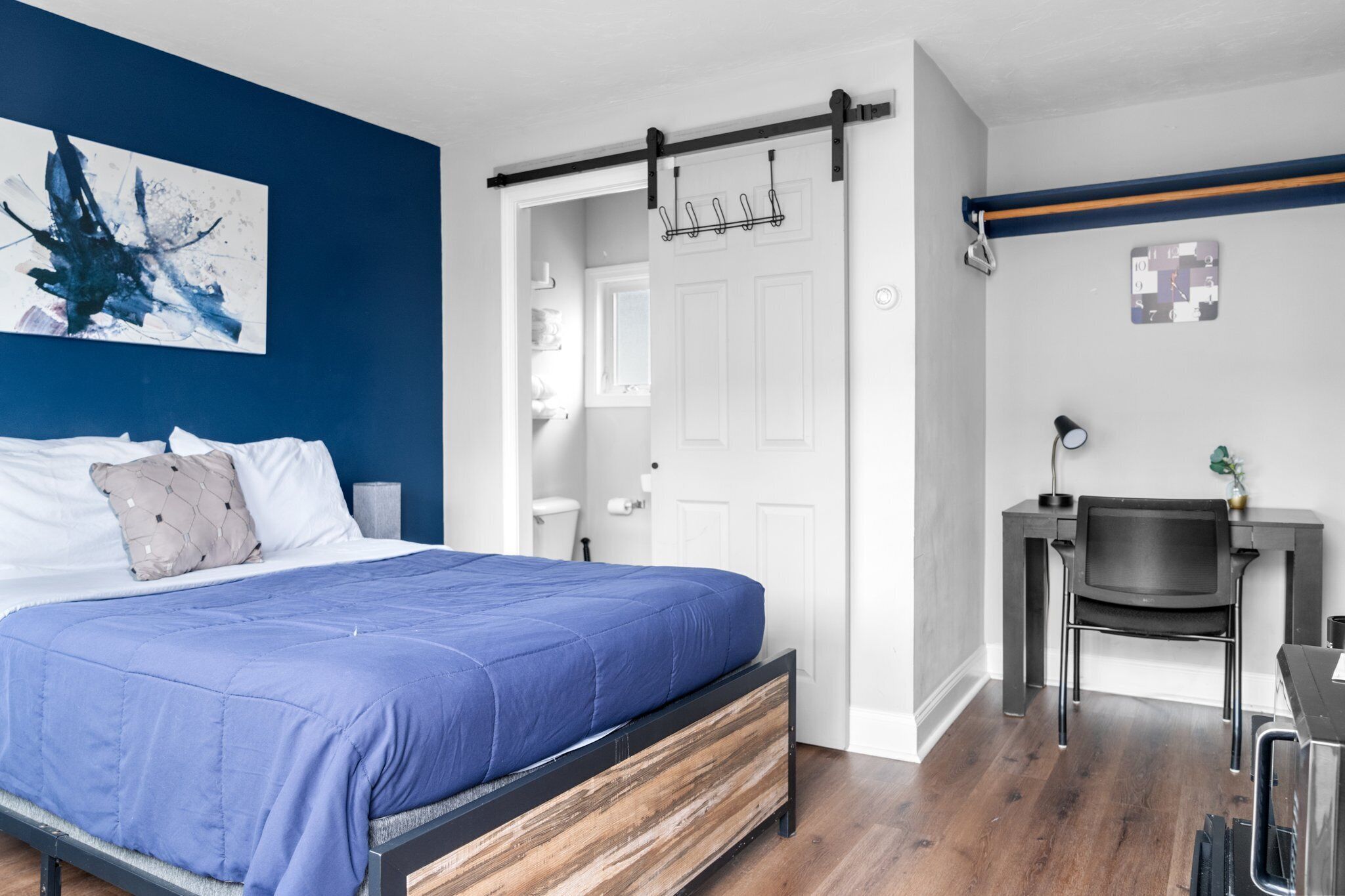 A bedroom with a bed, a desk, and a bathroom.
