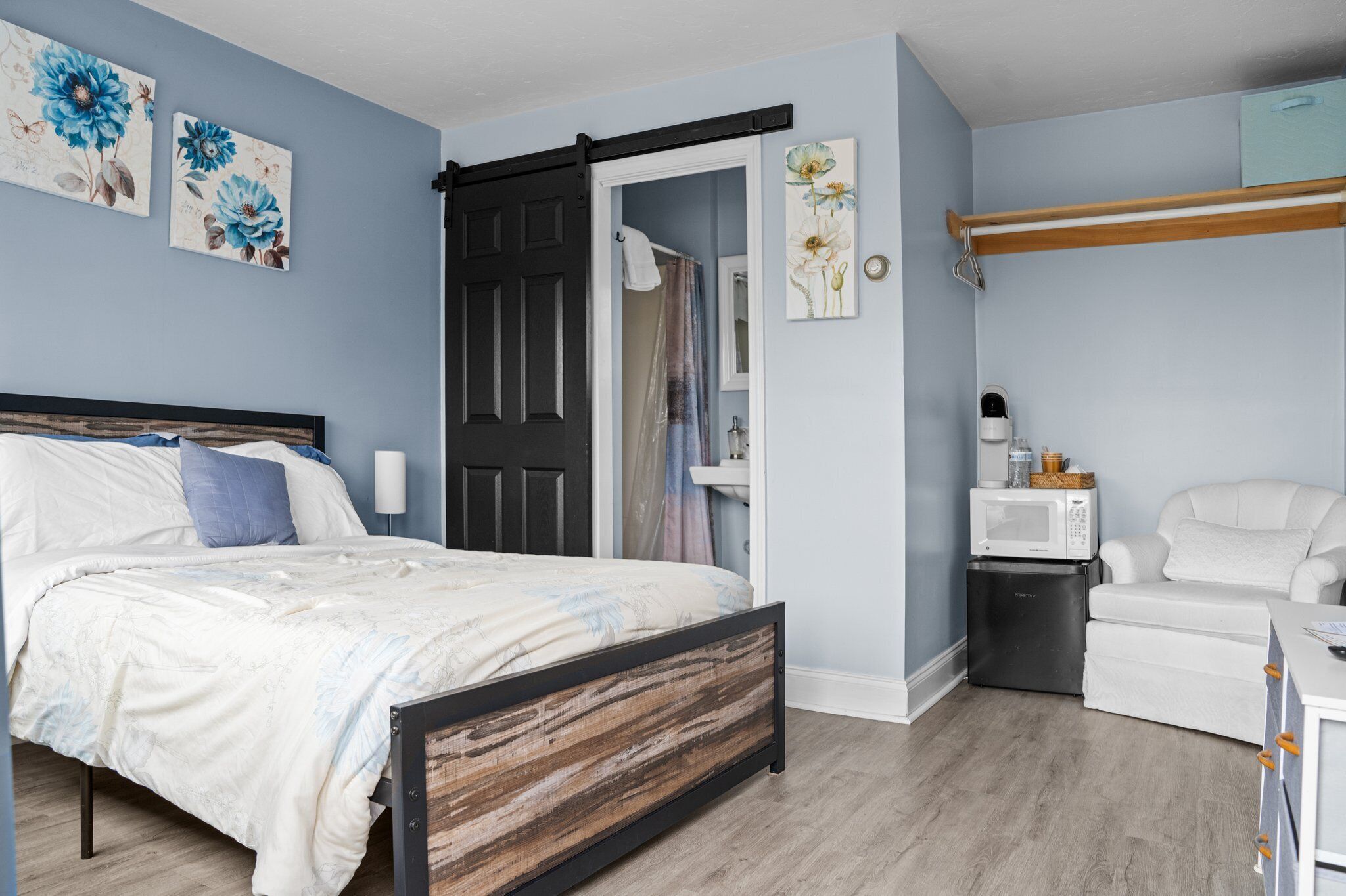 A bedroom with a bed, a black door, a white chair, a microwave, and a small refrigerator.
