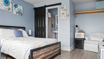 A bedroom with a bed, a black door, a white chair, a microwave, and a small refrigerator.