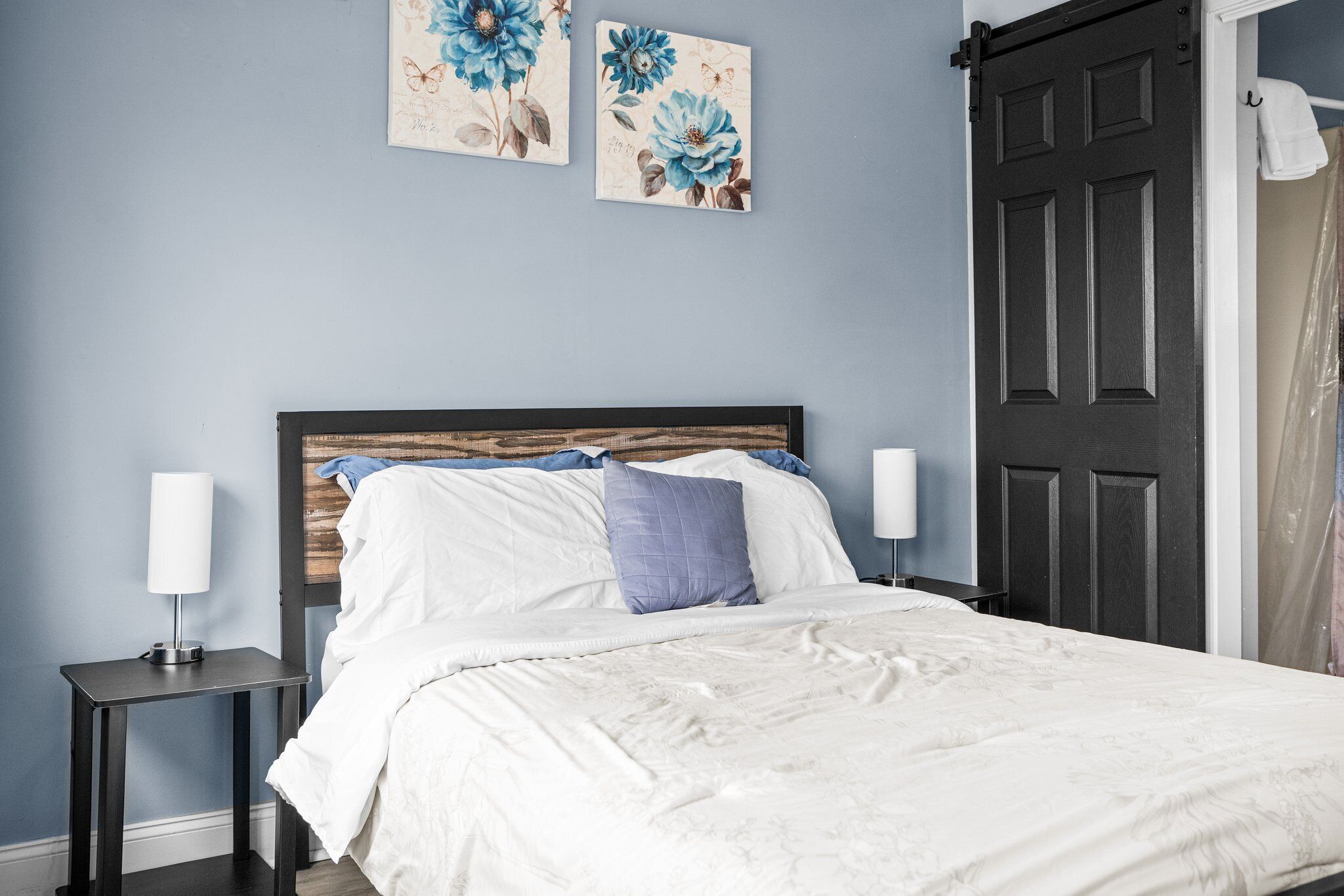 A bedroom with a bed, two nightstands, a headboard, and two wall-mounted floral artworks.