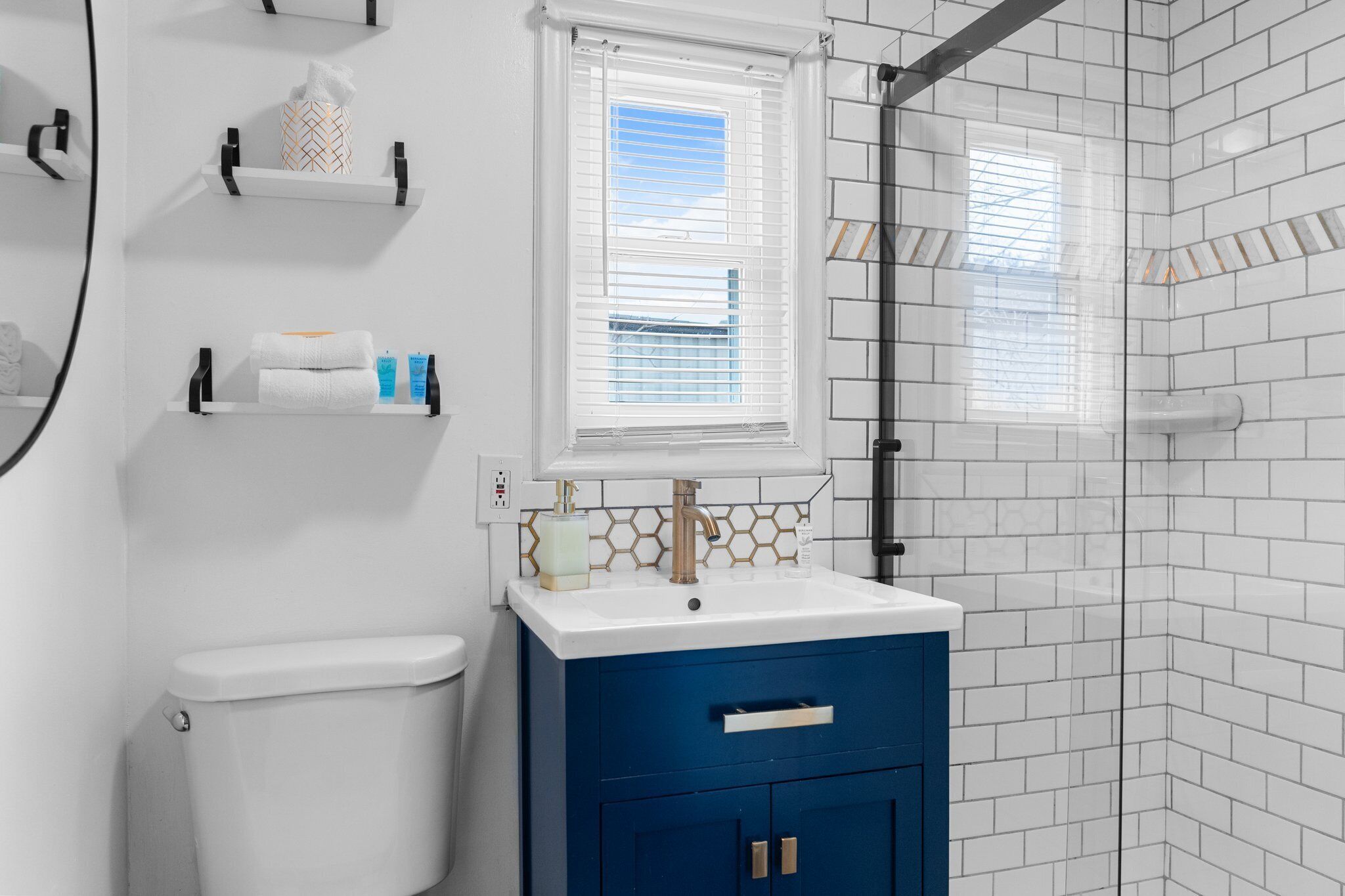 A bathroom with a white toilet, a blue vanity with a gold faucet, and a window with blinds.