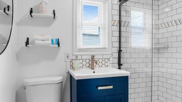 A bathroom with a white toilet, a blue vanity with a gold faucet, and a window with blinds.