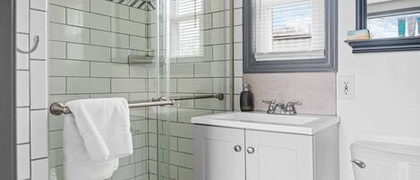 A bathroom with a glass shower enclosure, white tiled walls, a white sink, and a toilet.