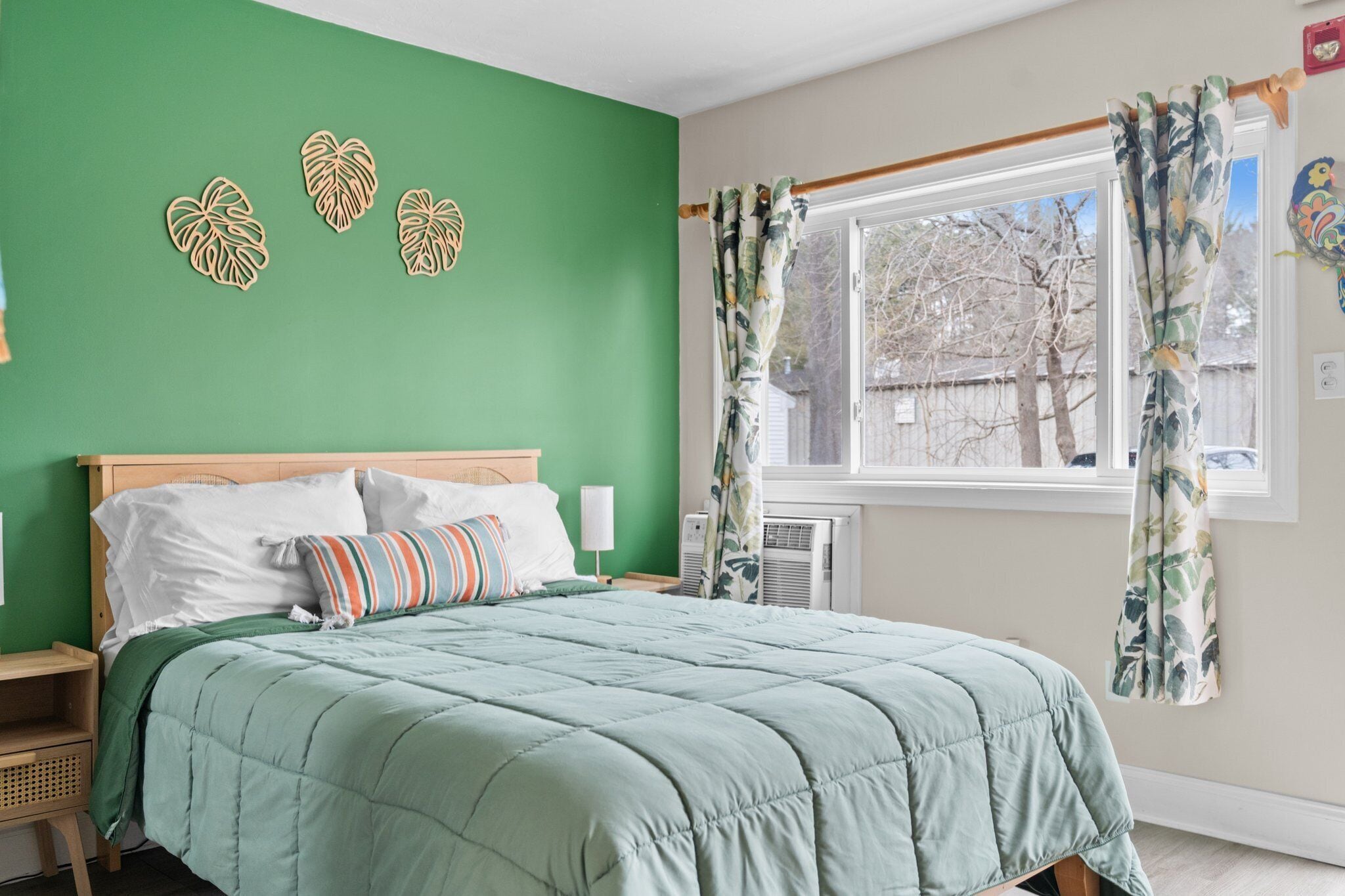 A bedroom with a green wall, a bed with a green quilt, and a window with floral curtains.