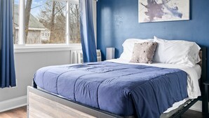 A bedroom with a bed, a window, and a blue wall. - Washington Park Motel (Norwell)