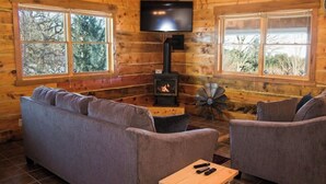 L’intérieur d’une cabane en rondins, avec un canapé, deux fauteuils, un téléviseur, une cheminée et un ventilateur.
