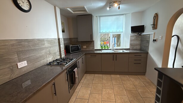 A modern kitchen with a gas stove, microwave, and a window with a view of flowers. - 3a Benson st (Ulverston)