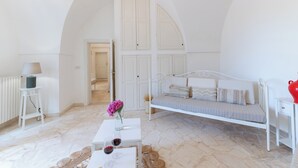 A white room with a bed, a small table with a vase of flowers, and a lamp. - Masseria Profilo 8, Emma Villas (Monopoli)