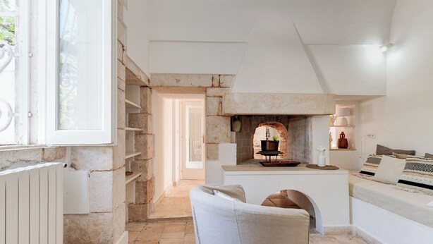 A narrow, stone-walled room with a fireplace, a small seating area, and a window. - Masseria Profilo 8, Emma Villas (Monopoli)
