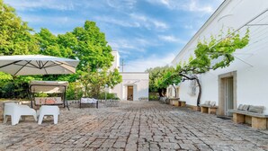 A cobblestone courtyard with outdoor seating, a pergola, and a white building with a door and windows. - Masseria Profilo 8, Emma Villas (Monopoli)