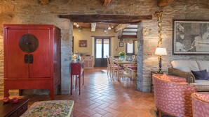 Ein rustikales Interieur mit einer Steinwand, Holzbalken, einem Essbereich mit Stühlen und einem Tisch sowie einem roten Schrank.