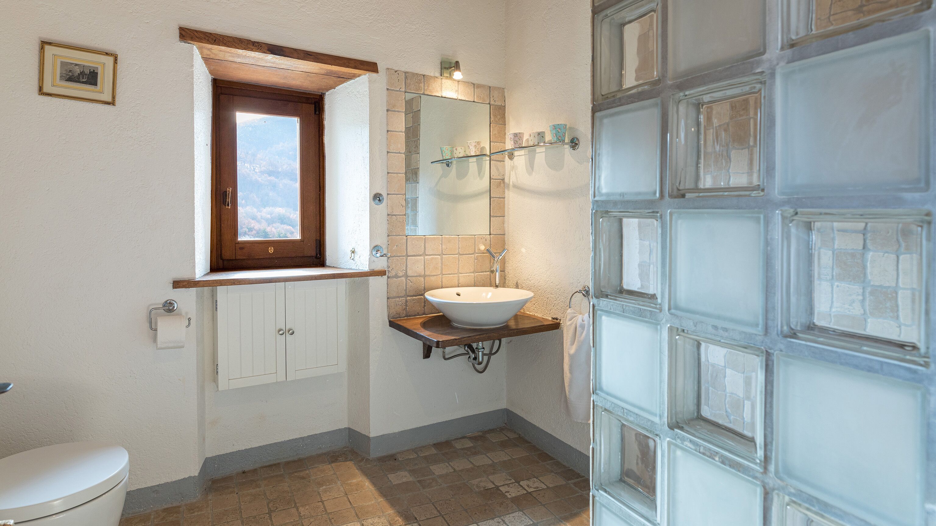 A bathroom with a toilet, a sink with a mirror, a window, and a door with glass panels.
