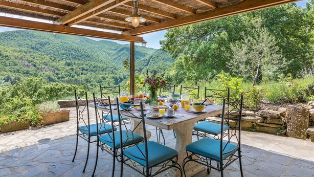 Ein Essbereich im Freien mit einem für das Frühstück gedeckten Tisch, umgeben von Steinmauern und Blick auf die Berge.