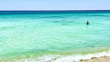 A beach with clear turquoise water, a sandy shore, and a person swimming.