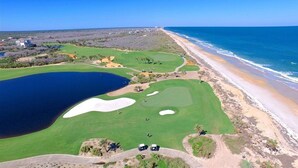 Ein Golfplatz mit einem großen Wasserspiegel, einem Strand und blauem Himmel.