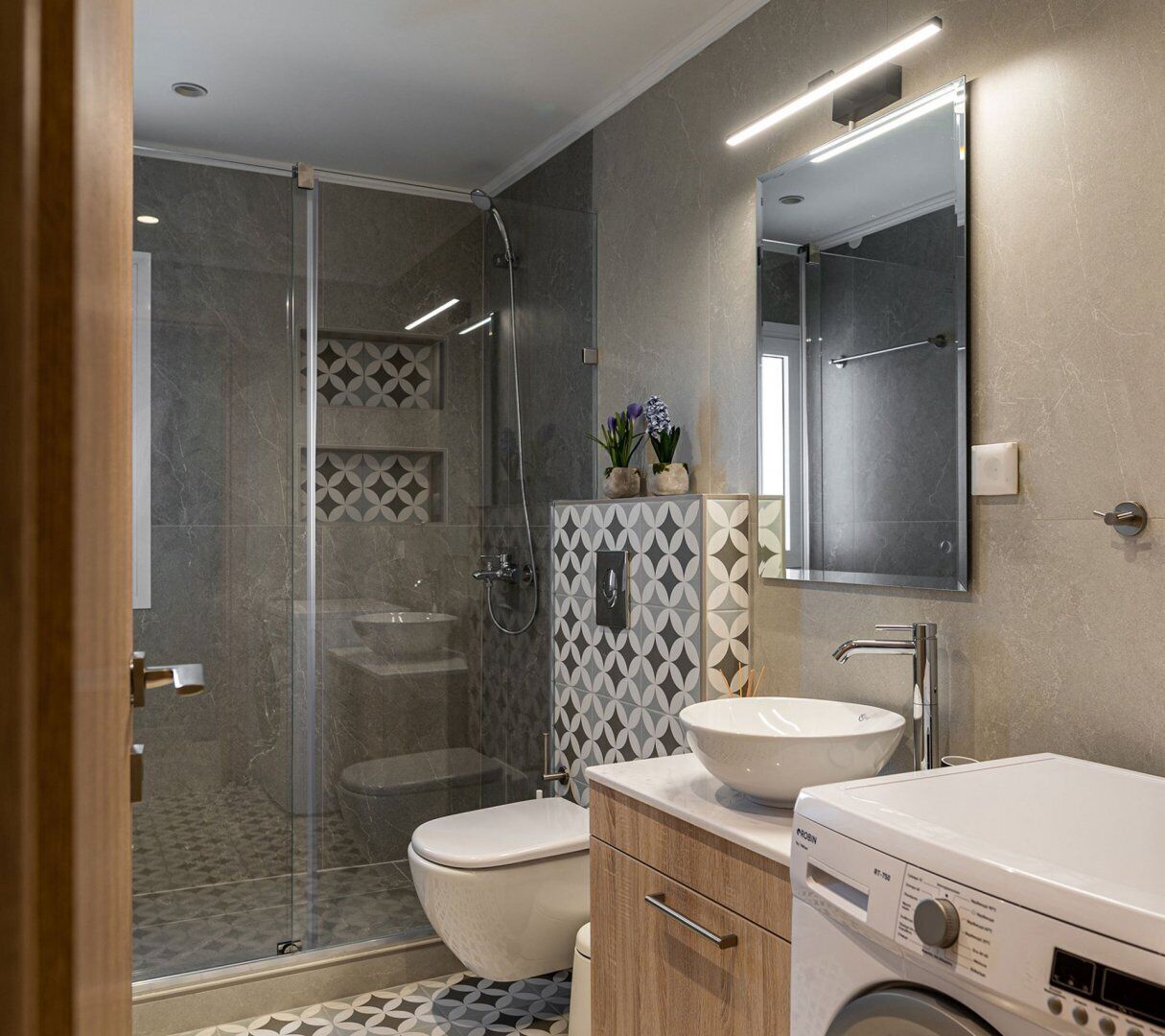 Un baño moderno con ducha de vidrio, inodoro, lavamanos y lavadora.