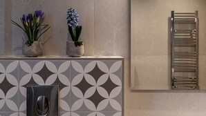 Un baño con toallero, un lavabo con grifo moderno y dos plantas en macetas sobre el mostrador.