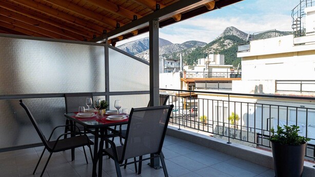 Un balcón con una mesa lista para comer, una planta en maceta y vistas a edificios y montañas.