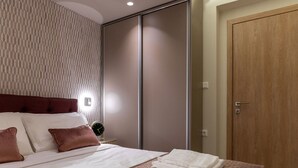 Un dormitorio con una cama, almohadas, una mesita de noche con un reloj, un armario y una puerta.