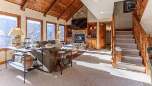 A spacious living room with a high ceiling, wooden beams, a stone fireplace, and a cozy seating area.