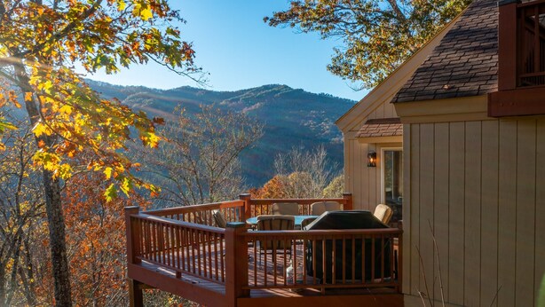 A wooden deck with outdoor seating, overlooking a mountainous landscape.