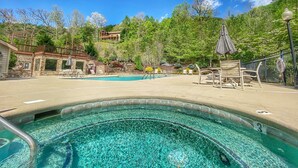 A clear swimming pool with lounge chairs and umbrellas, surrounded by trees and a stone building.