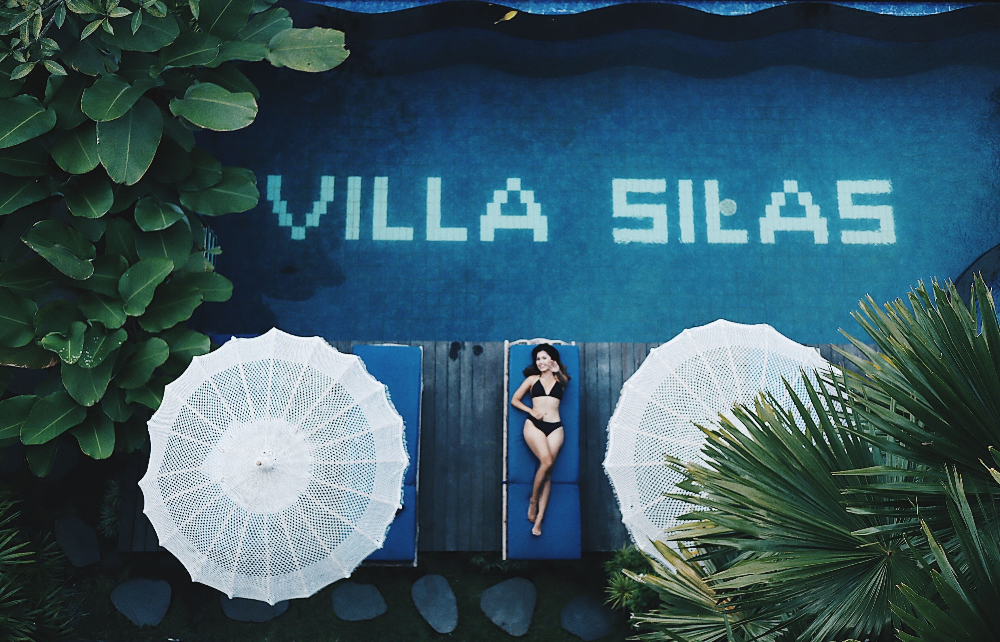 Eine Frau liegt auf einem blauen Liegestuhl vor einer Wand mit dem Schriftzug "VILLA SILAS".