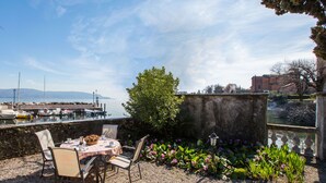 A patio with a table and chairs, a flower bed, and a view of the water and boats.