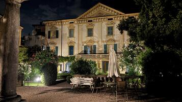 Ein historisches Gebäude mit klassischer Architektur, ein Innenhof mit Außenbestuhlung und ein gepflegter Garten.