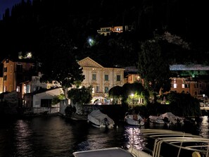 A historic building with classical architecture, situated by a calm body of water with boats docked nearby. - Charming Waterfront Apartment on Lake Garda (Toscolano Maderno)