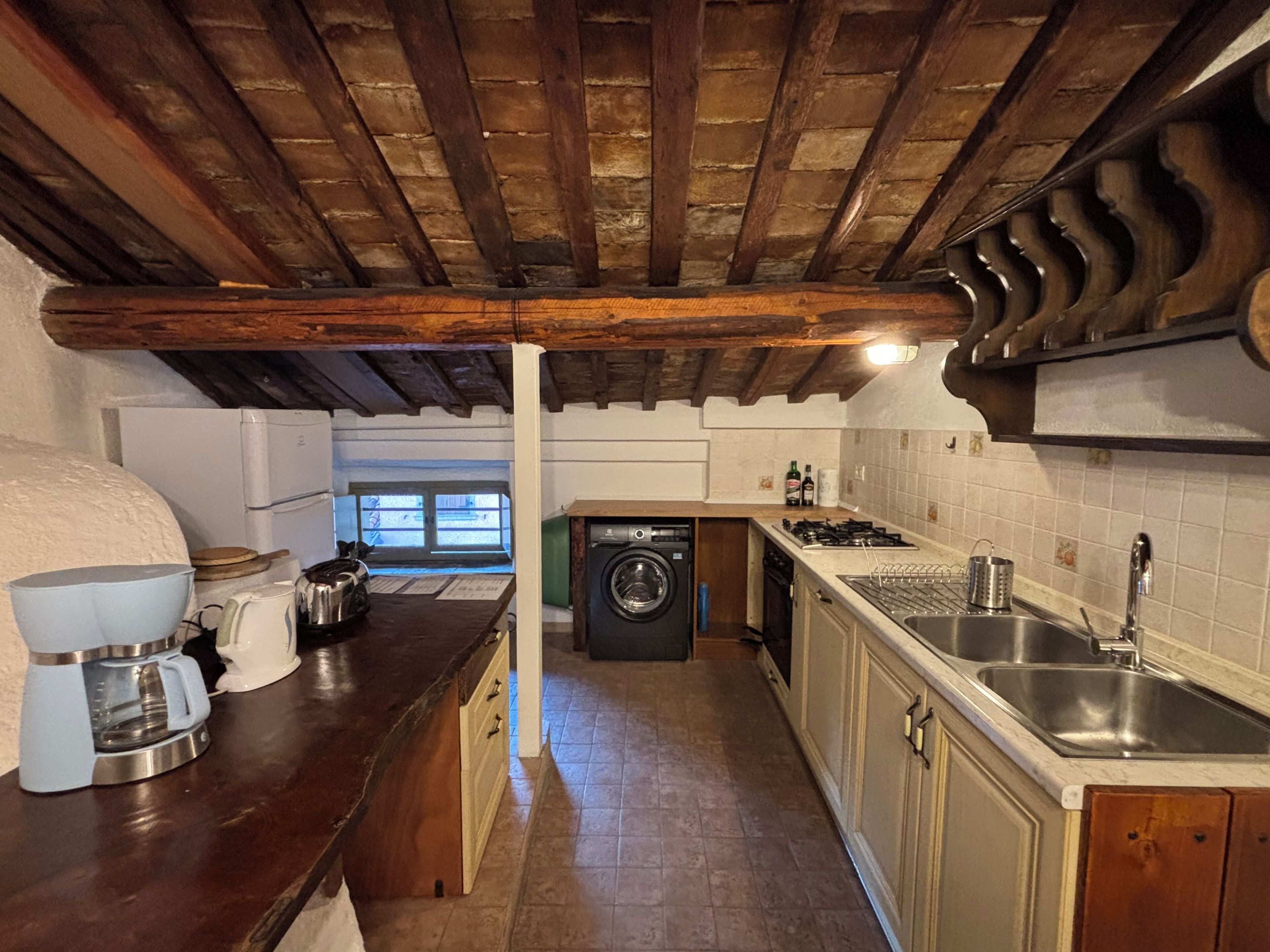 A kitchen with wooden beams, a washing machine, a coffee maker, and a sink.