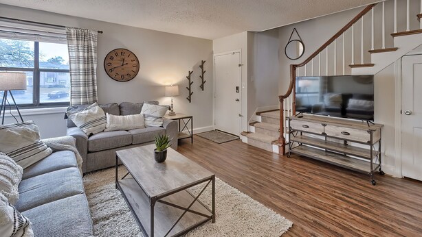 Ein Wohnzimmer mit einer Couch, einem Couchtisch und einer TV-Konsole. Eine Treppe mit einem Fernseher darauf.