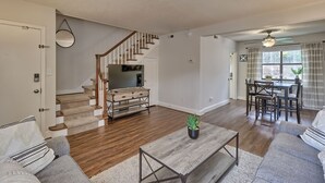 Ein geräumiges Wohnzimmer mit Holzdielen, einer Treppe, einem Essbereich und einem großen Fenster mit Vorhängen.