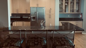 Una cocina moderna con armarios de madera, un refrigerador de acero inoxidable, encimera de mármol y comedor con barandilla de metal.