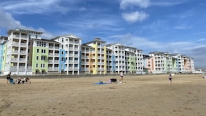 Una hilera de edificios coloridos de varios pisos con balcones, probablemente un hotel o resort, a lo largo de una playa arenosa bajo un cielo despejado.