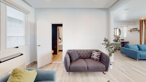 A modern living room with a grey sofa, a blue armchair, and a wooden floor. - Beautiful Gem In The Heart of Condado - 3 mins from the beach! (San Juan)