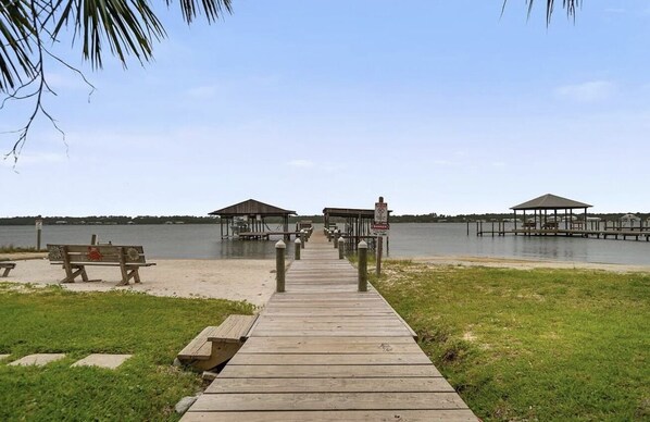 A wooden pier leading to a dock area with two gazebos and a bench on the sand.