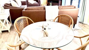 Ein Wohnzimmer mit einem runden Glastisch, umringt von Korbstühlen, einem braunen Sofa und einem Fernseher.