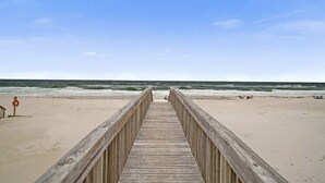 Eine hölzerne Steg, der zu einem Strand mit Wellen im Hintergrund führt.