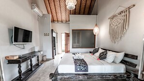 A bedroom with a large bed, a TV, a console table, and a macrame wall hanging. - LONG TERM Rent Only - Budget Friendly Private Room (Ubud)
