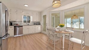 A modern kitchen with white cabinetry, a stainless steel refrigerator, and a dining area with a table and chairs. - Pool House/ 9beds/4Ba/ Kings/ Billiard/ Air Hockey (Lawrenceville)
