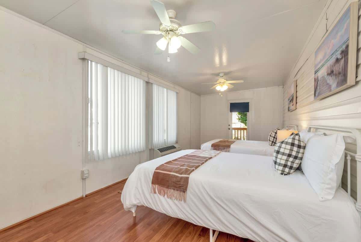 A bedroom with two beds, a ceiling fan, and a window with blinds.