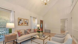 A spacious living room with a sofa, two armchairs, a coffee table, and a side table with lamps. There are two framed pictures on the wall, a window with blinds, and a door leading to another room. - Pool House/ 9beds/4Ba/ Kings/ Billiard/ Air Hockey (Lawrenceville)