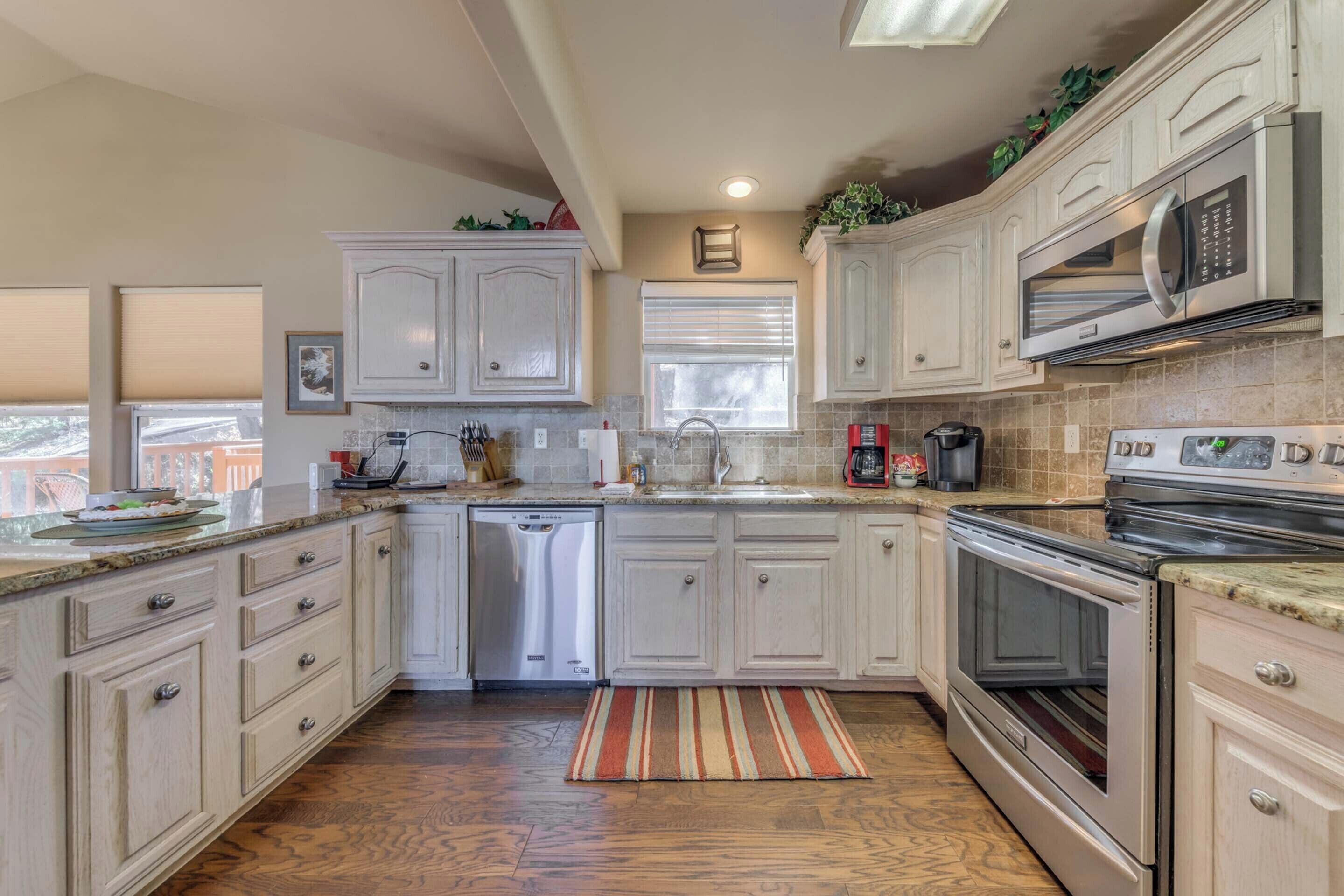 A kitchen with white cabinets, stainless steel appliances, a dishwasher, and a striped rug.