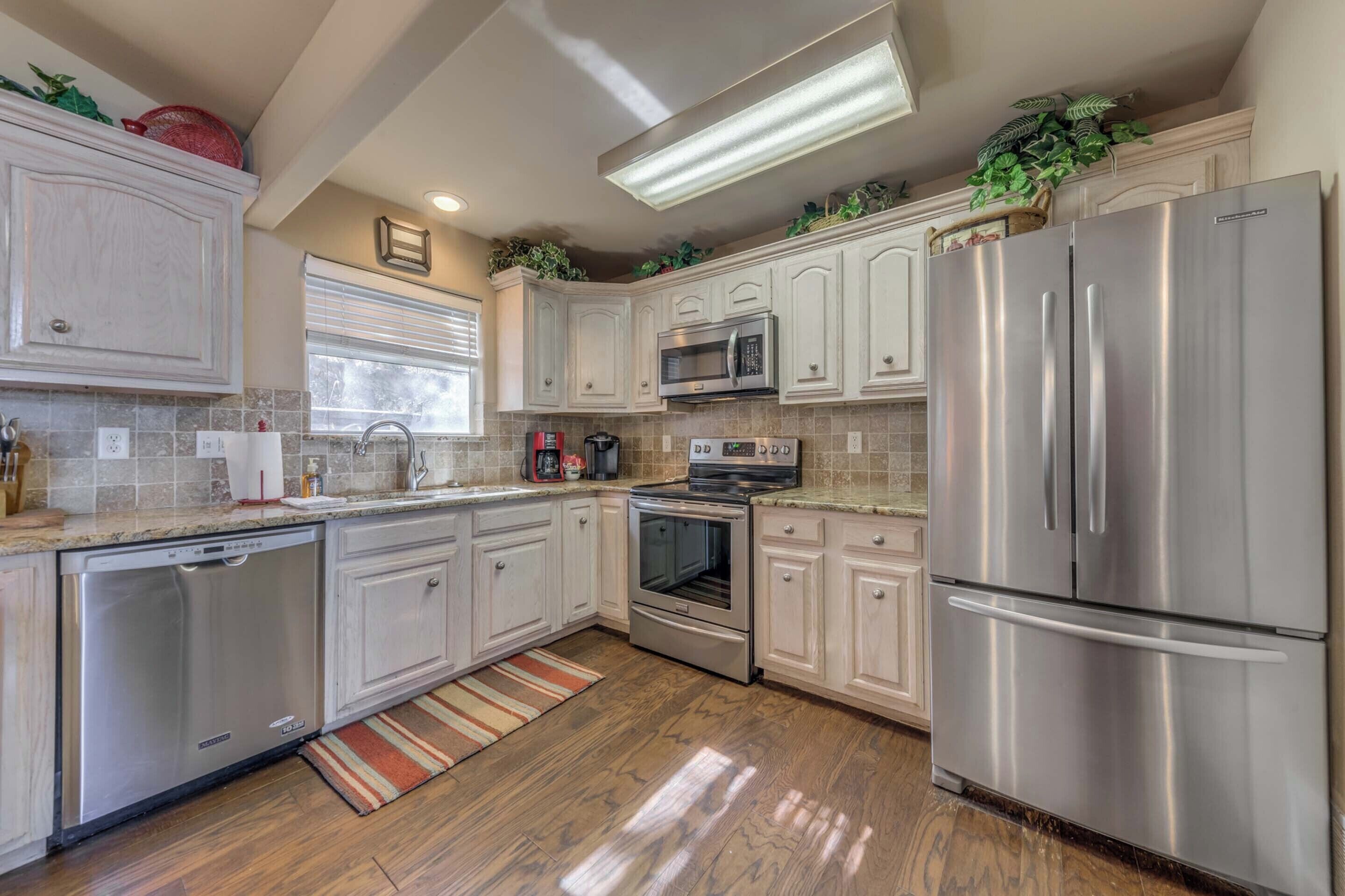 A modern kitchen with stainless steel appliances, white cabinetry, and a wooden floor.