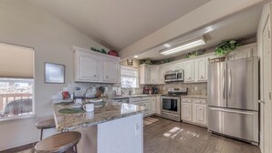 Una cocina moderna con armarios blancos, electrodomésticos de acero inoxidable y una isla central con taburetes.