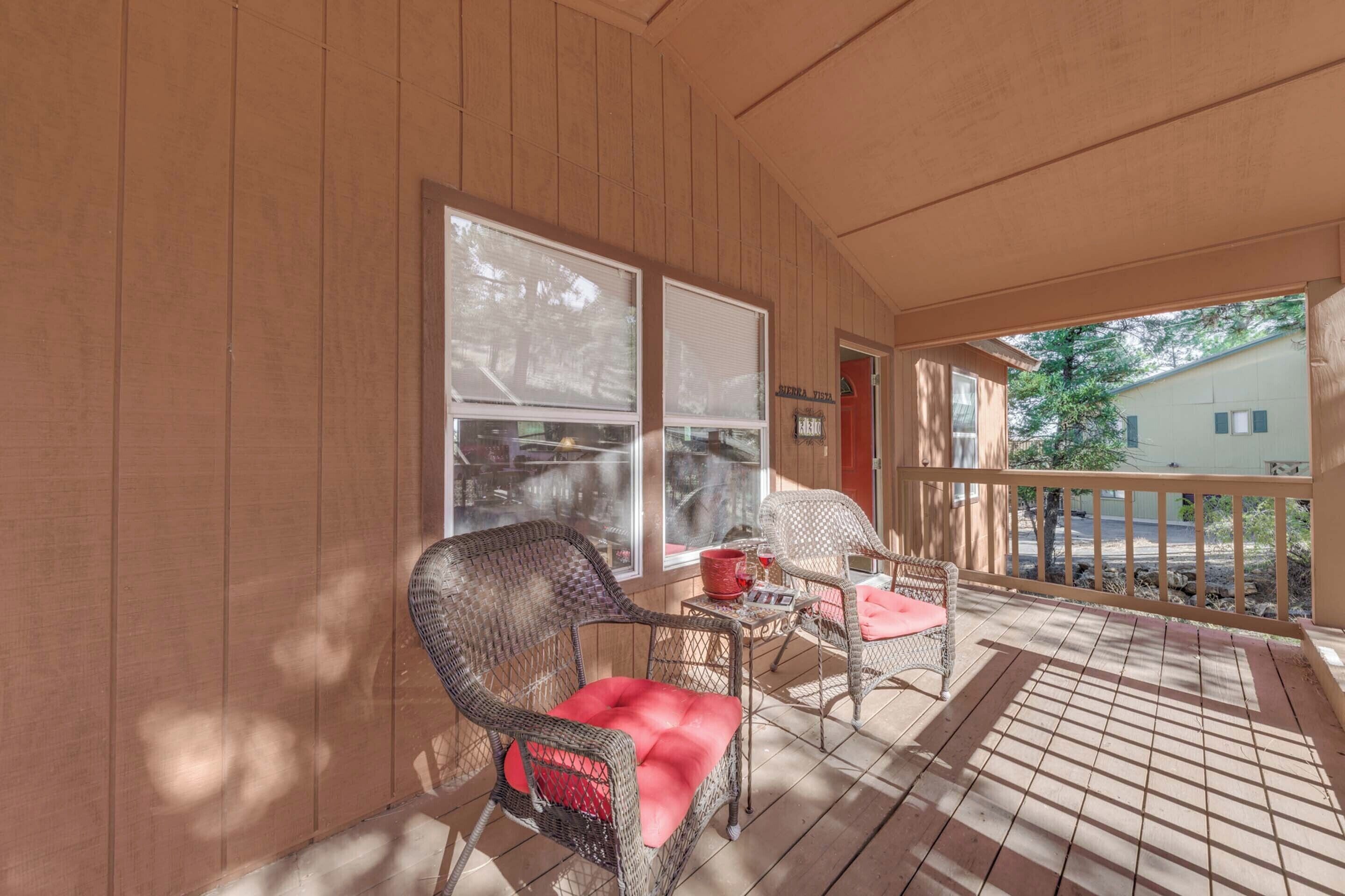 A covered porch with wicker chairs and a table, large windows, and a view of a residential area.