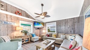 A living room with a wooden wall, a ceiling fan, a TV, and a sofa set. - Diving Dolphin by Silver Sands Vacation Rentals (Port Aransas)