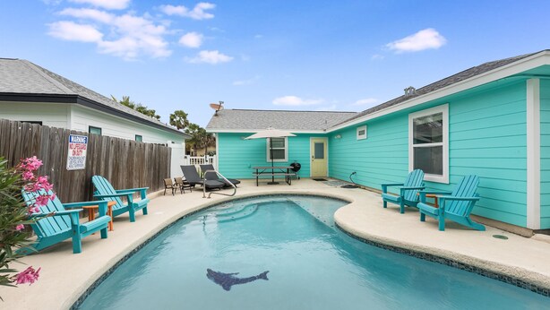 A swimming pool with a shark silhouette, surrounded by turquoise chairs and a wooden fence. - Diving Dolphin by Silver Sands Vacation Rentals (Port Aransas)