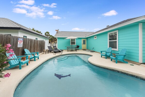A swimming pool with a shark silhouette, surrounded by turquoise chairs and a wooden fence. - Diving Dolphin by Silver Sands Vacation Rentals (Port Aransas)